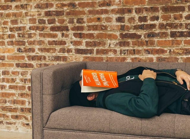 person sleeping on a sofa with a book over face